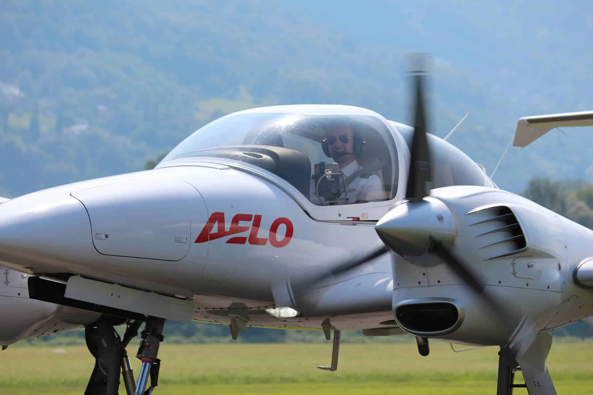 Diamond DA42 twin-engine aircraft with AELO logo, pilot in cockpit.