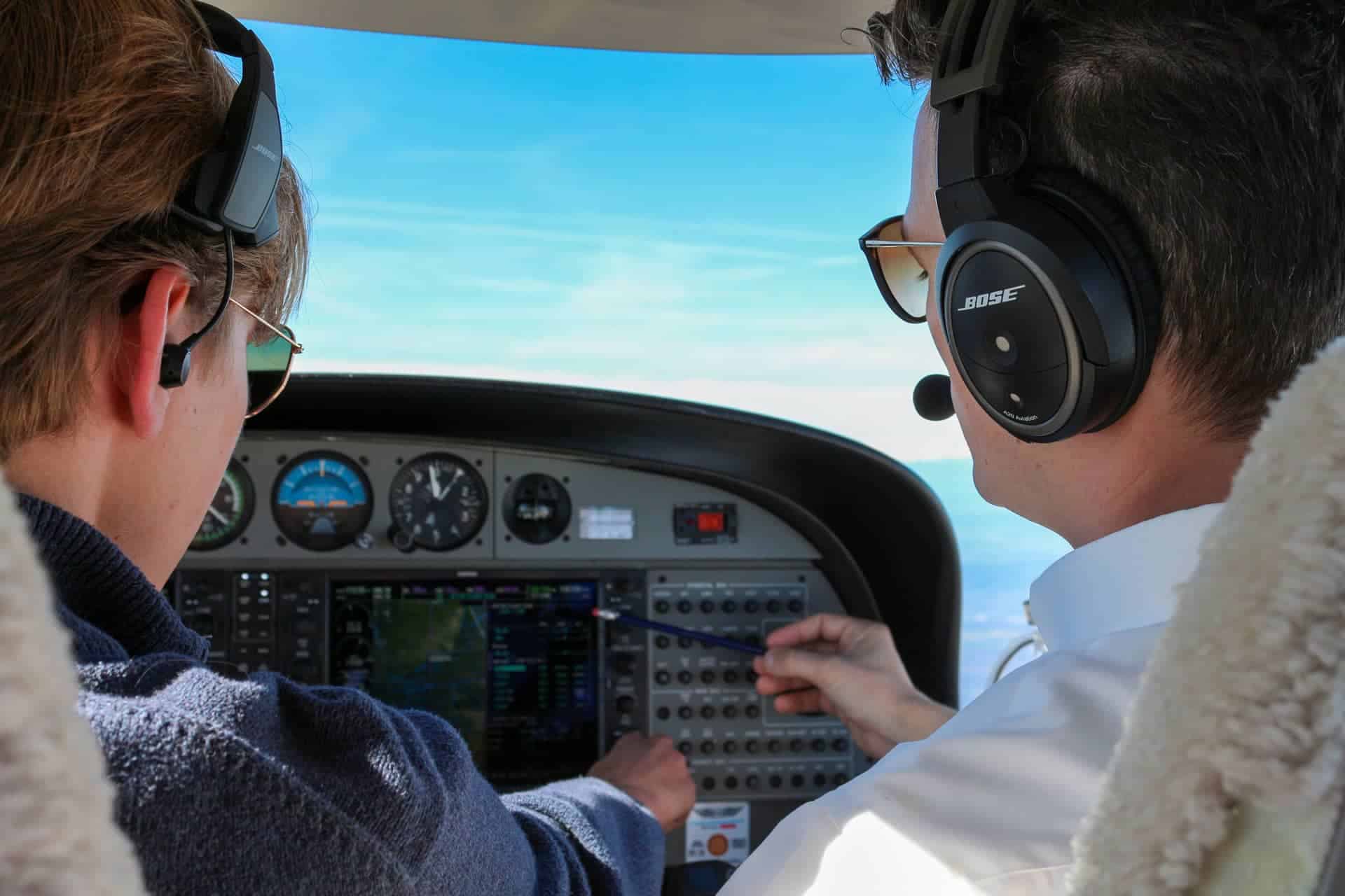 Piloto instructor y estudiante en cabina de avión, instrumentos de vuelo y controles.