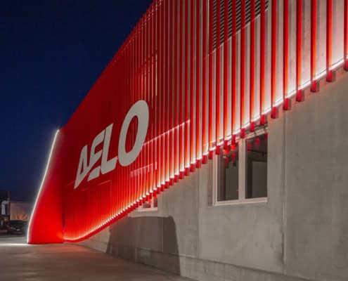 Fachada moderna de Aelo Swiss Academy con iluminación roja y el logo de la academia.